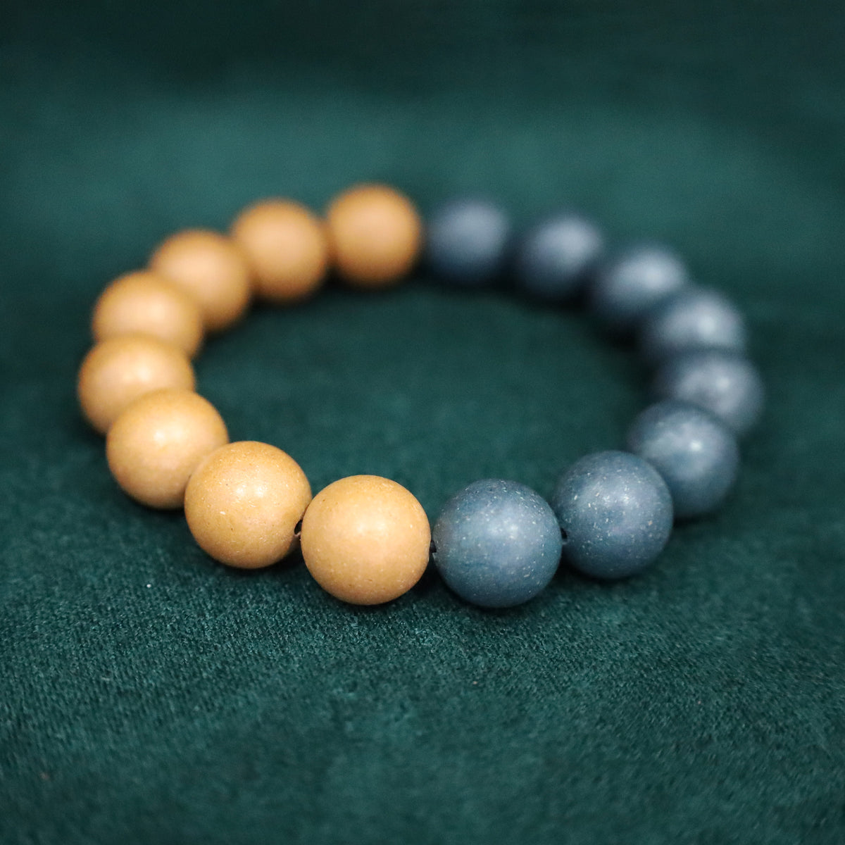 Yin-yang style herbal incense bead bracelet in warm apricot and cool blue-gray tones on deep green cloth