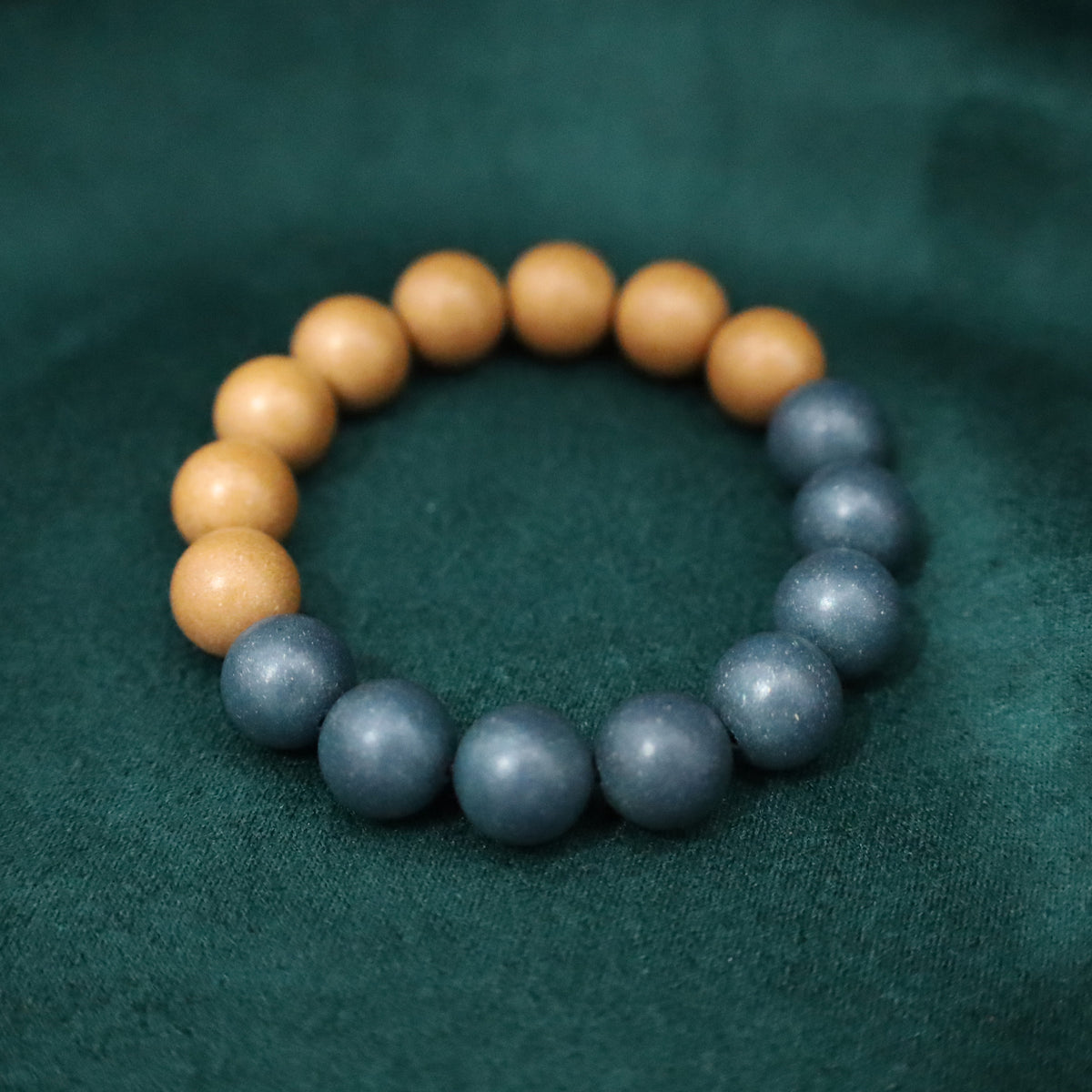 Handmade dual-formula incense bead bracelet, half warm beige beads and half gray-blue beads, arranged in a circle on dark green fabric