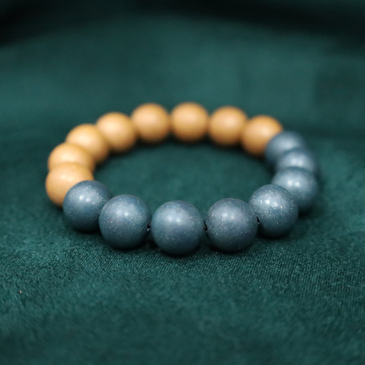Two-tone handmade herbal incense bead bracelet, half warm apricot-beige beads and half misty blue-gray beads, looped on dark green fabric