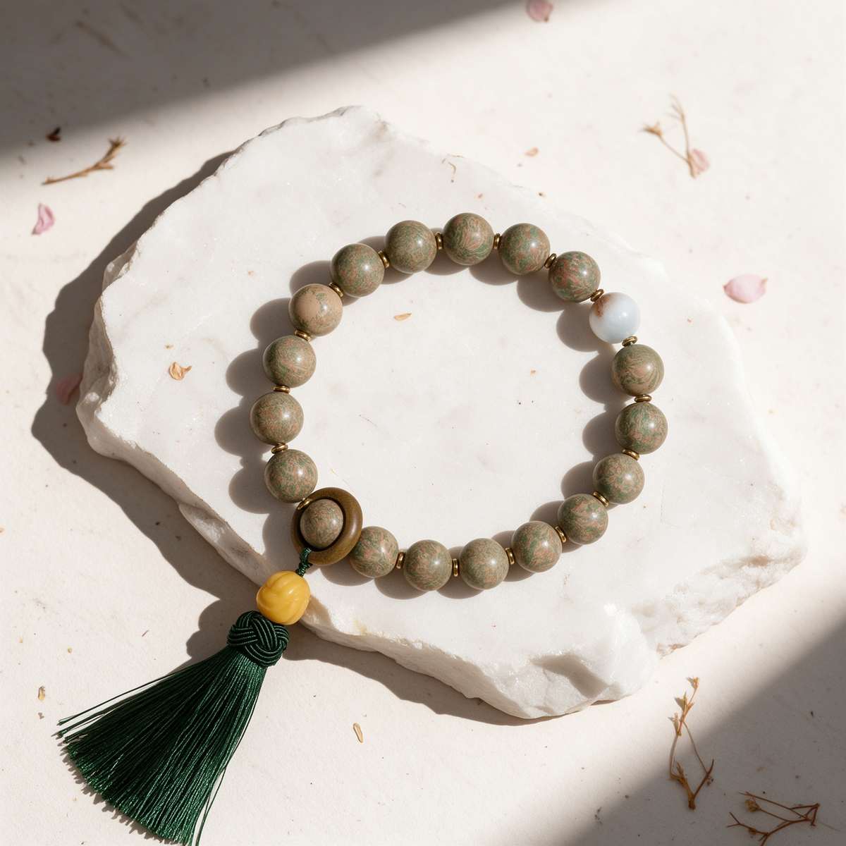 Tang Sancai-style mottled incense bead meditation mala with brass spacers, wooden runner ring, honey-yellow pumpkin bead and dark green tassel, arranged on a white stone slab
